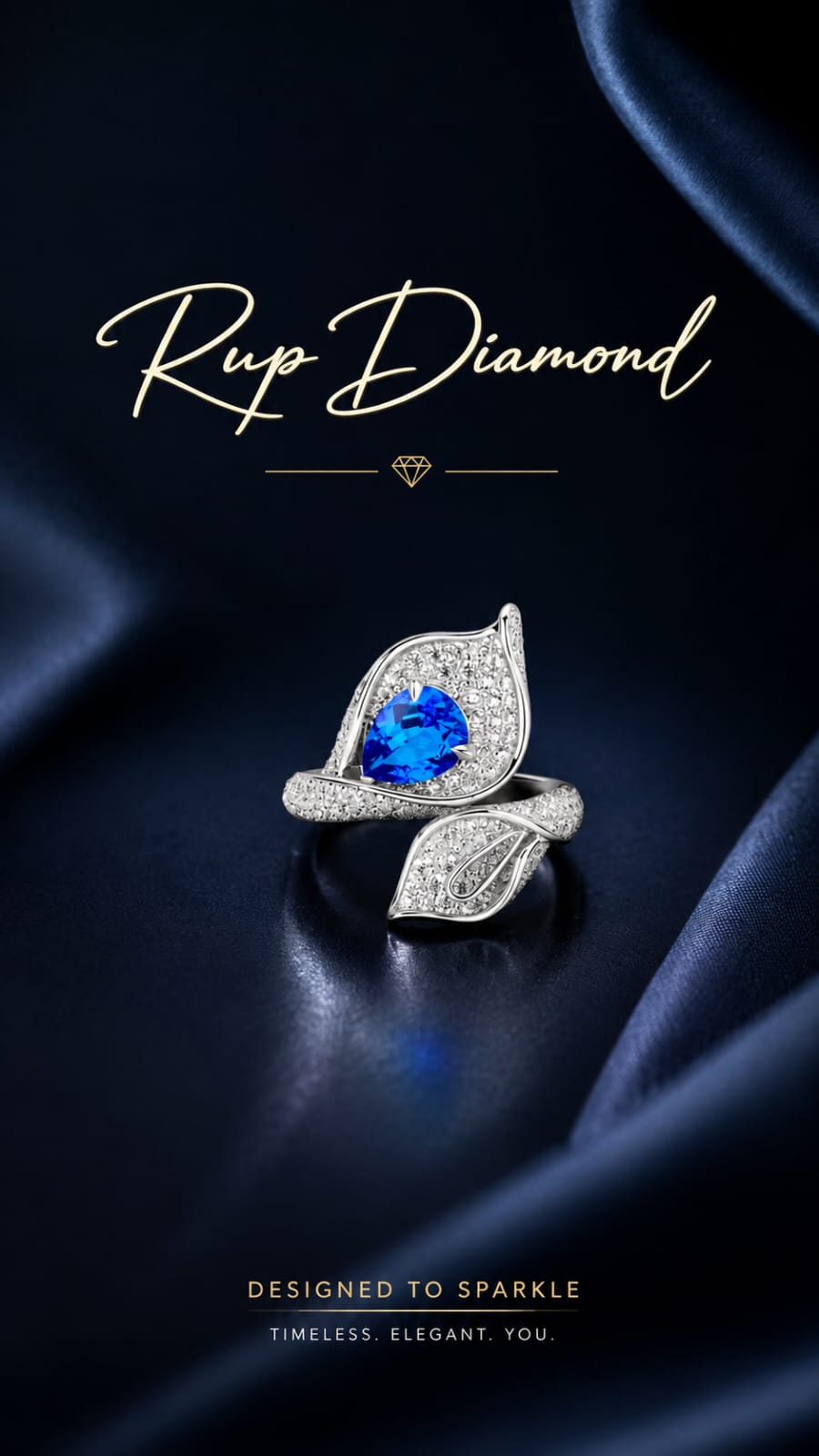A silver-toned leaf-shaped ring with a vivid blue teardrop gemstone and pavé-set clear stones, displayed on dark navy draped fabric. The brand name 'Rup Diamond' appears in gold script at the top, with the tagline 'DESIGNED TO SPARKLE' at the bottom.